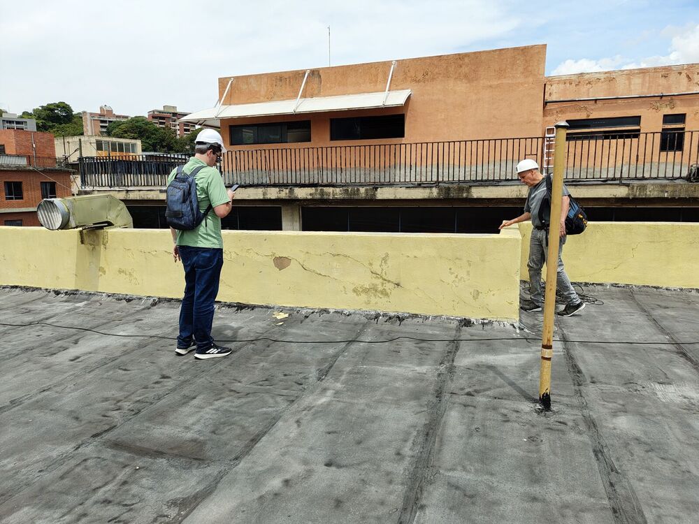 Técnicos de Corporación 3JC levantando con mira topográfica la azotea de un edificio en Caracas, junto a un parapeto agrietado